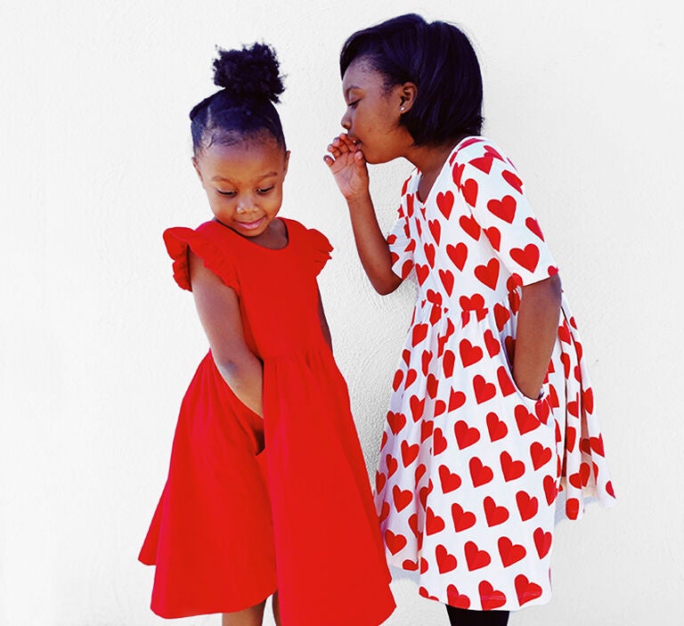 A girl wearing a Valentine's Day heart dress whispering to her sister in a red dress