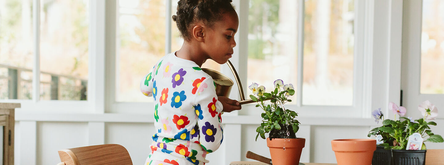 Image of children watering plants wearing Hanna Andersson
                pajamas.