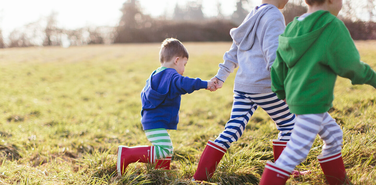 Image of children walking through a field dressed in Hanna
                Andersson clothing and boots.