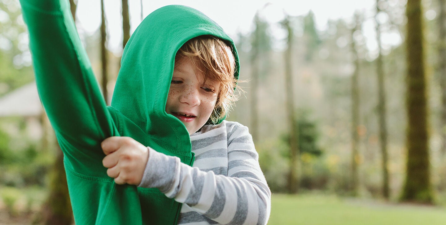 Boy in grey and white stripe pajamas putting on green hoodie