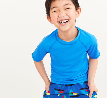 boy in a blue sun-blocking rash guard and boat printed shorts. shop now boy in a blue sun-blocking rash guard and boat printed shorts. shop now