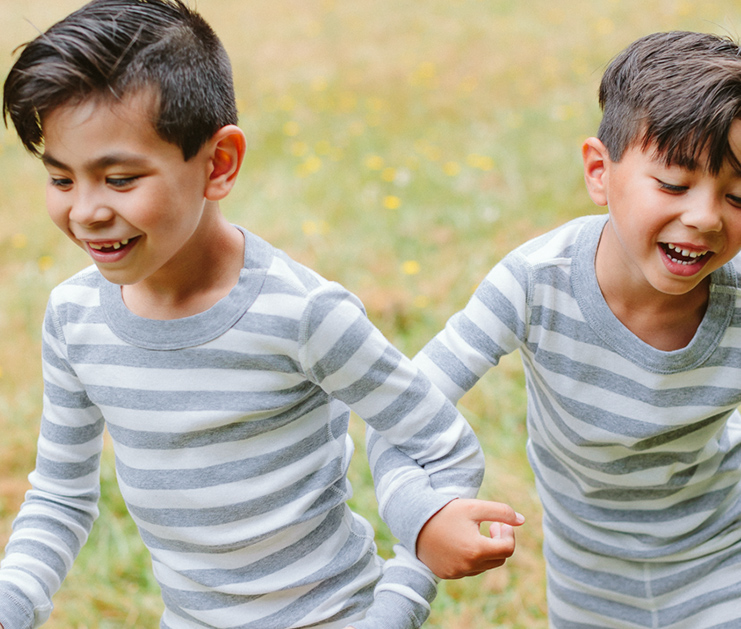 Image of sibling brothers playing smiling in a field wearing Hanna Andersson clothing.
