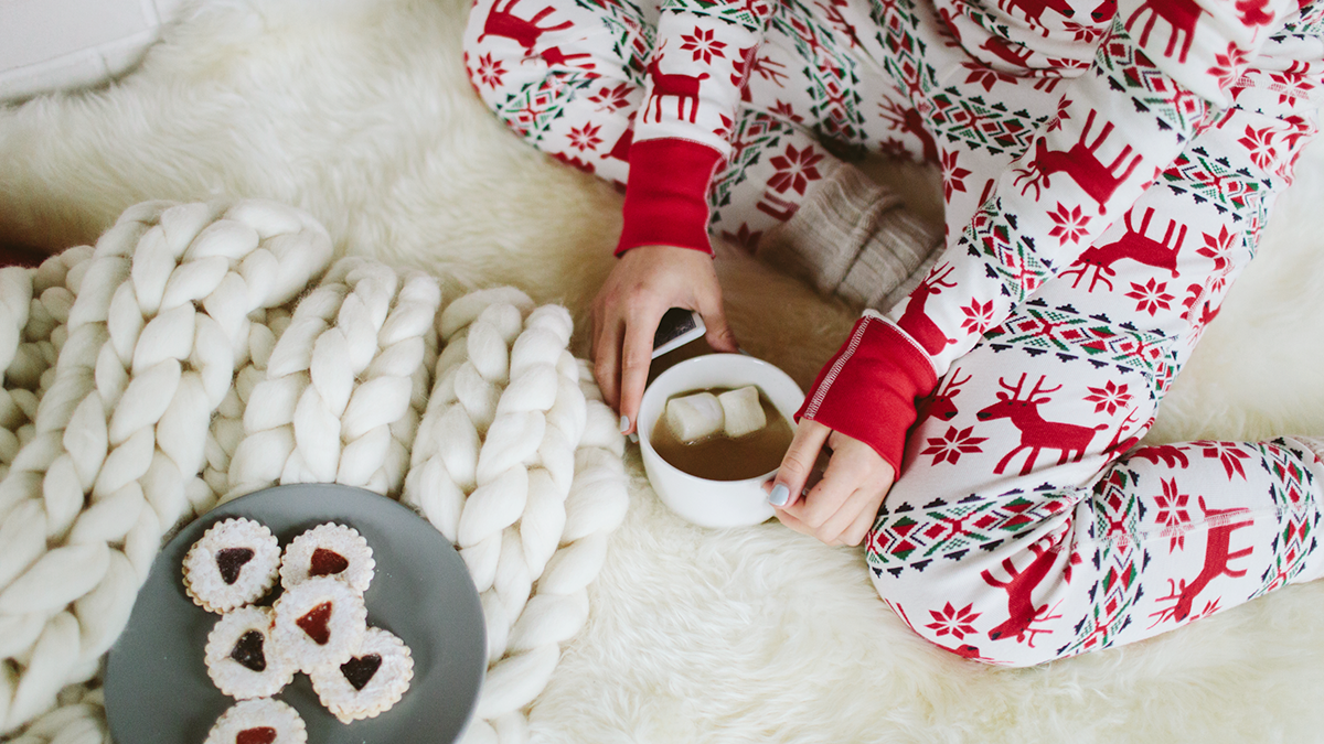 Woman in holiday pajamas drinking hot cocoa with a plate of cookies