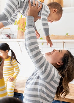 mom holding up baby wearing matching stripe grey pajamas